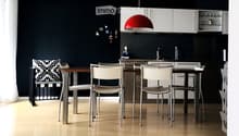 Modern dining area with a wooden table, white chairs, and a sleek kitchen area featuring white cabinets and a red pendant light.