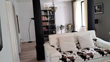 Elegant living room with white leather sofa, cowhide throw, glass coffee table, bookshelf, floor lamp, and chandelier.