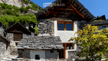 Stone house with wooden doors and windows, situated in a mountainous area with a stone staircase leading to the entrance.