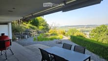 Outdoor patio with tiled floor, table and chairs, grill, and scenic view of greenery and countryside.