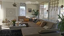 Modern living room with a large sectional sofa, coffee table, side table, pendant light, wall art, and plants.