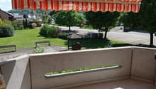Balcony with tiled floor, stone railing, and striped awning, overlooking a green lawn and residential area.