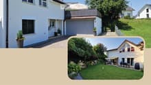 Two-story white house with a tiled roof, multiple windows, a garage, and a balcony with an umbrella. The surrounding area includes a well-maintained garden, a raised ground floor, and a parking area.