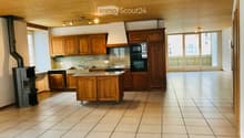 Bright kitchen with wooden cabinets, a central island, and modern appliances including an oven and microwave. Features a tiled floor, large windows, and a wood-burning stove.