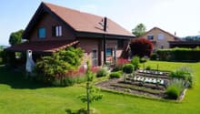 A well-maintained garden with a lawn, flower beds, a small tree, and a patio area with a table and chairs near the house.