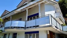Two-story house with white exterior, blue shutters, balcony with metal railing, and outdoor patio area with a table and chairs.