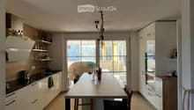 Modern kitchen with white cabinets, a dining table with chairs, and a view through large windows.