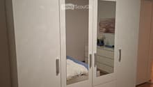 Modern bedroom with large white wardrobe, bed with blue bedding, nightstand, and mirror on the wardrobe door.