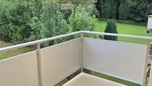 Balcony with white privacy screens, metal railing, and a view of a green garden and trees.