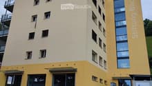 Modern multi-story building with yellow and beige facade, large windows, and a balcony on the upper floor.
