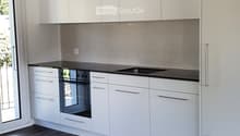 Modern kitchen with white cabinets, black countertops, integrated oven, and sink.