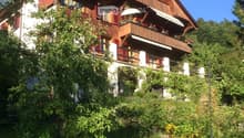 A two-story wooden house with red shutters, balconies, and a well-maintained garden.