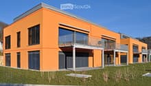 Modern two-story building with orange facade, large windows, balconies, and a garage entrance.