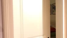Open doorway leading to another room, with visible interior elements like a bed and artwork in the background.