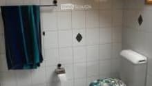 Bathroom with white tiled walls and floor, a toilet, a bathtub, and a towel hanging on the wall.