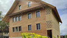 Two-story house with a brown facade, multiple windows, and a decorative wooden lattice on one side.