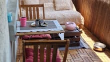 Balcony with wooden decking, sofa, small table, chairs, and potted plants.