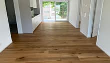 Empty room with light wooden flooring, white walls, and a sliding glass door leading to a balcony.