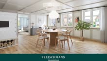 Bright, modern living and dining area with wooden flooring, large windows, a round dining table with four chairs, a sofa, a pendant light, a fireplace with stacked logs, and a potted plant.