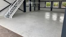 Empty garage with concrete floor, white metal staircase leading up, large windows, and industrial-style doors.