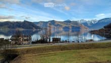 Scenic lakeside view with calm water, distant mountains, and a few houses along the shore.