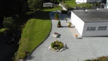 Aerial view of a modern house with a well-maintained garden, gravel driveway, and landscaped greenery.