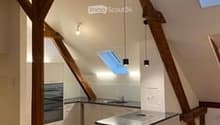 Bright, open-plan attic kitchen with exposed wooden beams, skylights, and modern appliances.
