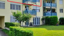 Multi-story residential building with light yellow facade, multiple balconies, and surrounding greenery.