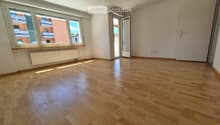 Empty room with wooden flooring, large windows, and a radiator. No furniture or equipment present.