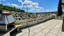 Roof terrace with concrete tiles, low stone walls, and a view of a town and surrounding hills.