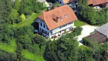 Aerial view of a house with a red roof, surrounded by trees and plants, with a driveway leading to it.