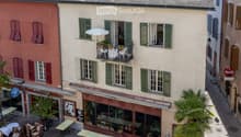 Courtyard with outdoor seating, tables, chairs, potted plants, and a small balcony with greenery and an umbrella.