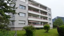 Modern multi-story apartment building with balconies, large windows, and a well-maintained lawn in front.