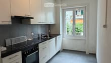 Modern kitchen with white cabinets, black countertops, and stainless steel appliances, including an oven and range hood. The space features a large window with a view of greenery outside.
