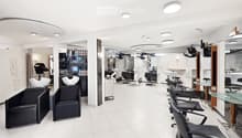 Modern salon with white tiled floors, multiple black and white chairs, mirrors, shelves with hair products, and a reception area with a glass table.