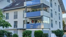 Modern two-story house with multiple balconies, large windows, and a well-maintained garden.