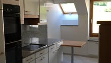 Modern kitchen with white cabinets, granite countertops, induction stove, built-in oven, and a small wooden table.