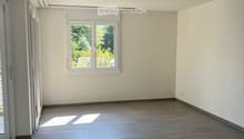 Empty room with light grey tiled floor, white walls, and a window with white frame. Sunlight streams in from the window, casting shadows on the floor.