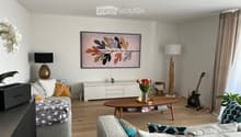 Living room with sofa, coffee table, TV, center table, speaker, white walls, flooring, plants, lamp, cabinet, artwork, remote control