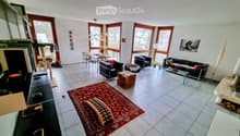 Bright living room with large windows, tiled floor, red rug, sofa, coffee table, cat tree, dining table, and chairs.