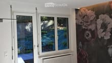 Empty room with white walls, large windows, radiator, and a floral wallpaper mural on one wall.