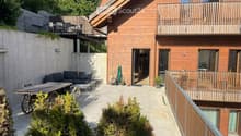 Outdoor patio area with a wooden table, sofa, chairs, and a small balcony with additional seating.