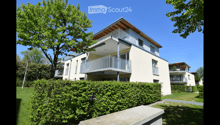 Modern two-story residential building with balconies, surrounded by greenery and a well-maintained lawn.