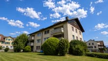 A multi-story residential building with balconies, surrounded by well-maintained green lawns and trees.