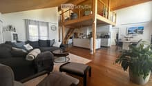 Open-concept living and dining area with wooden floors, a grey sectional sofa, coffee table, dining table, and kitchen area with white cabinets and appliances.