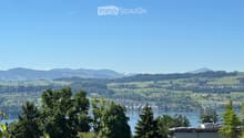Panoramic view of a lake surrounded by lush green hills and distant mountains under a clear blue sky.