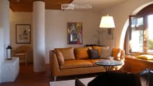 Cozy living room with leather sofa, coffee table, artwork on the walls, and a fireplace. The room has a warm, inviting atmosphere with natural light coming in through the windows.