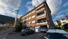 Modern multi-story building with balconies, garage, and several parked cars in front.
