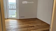 Empty room with wooden flooring and white walls, featuring a large window with a view of the outside.