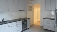 Modern kitchen with white cabinets, black granite countertops, stainless steel sink and oven, and a doorway leading to another room.
